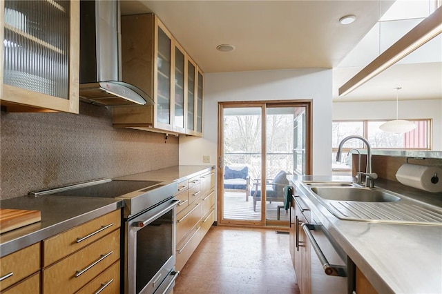 kitchen featuring wall chimney exhaust hood, appliances with stainless steel finishes, glass insert cabinets, decorative light fixtures, and a sink