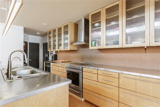 kitchen with electric stove, glass insert cabinets, wall chimney range hood, stainless steel counters, and a sink