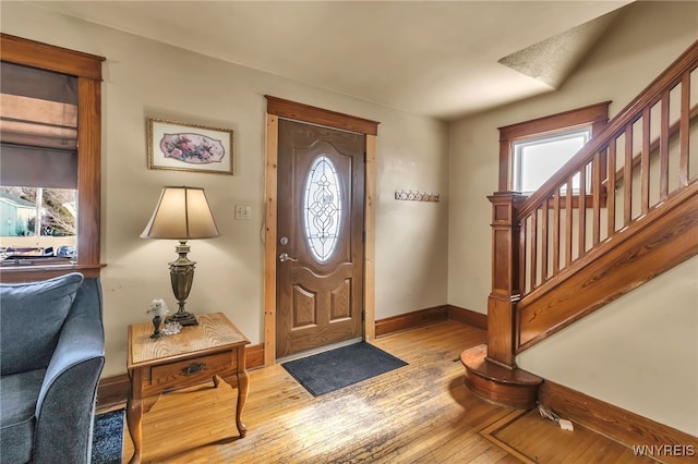 foyer entrance with light wood-style floors, baseboards, stairway, and a wealth of natural light