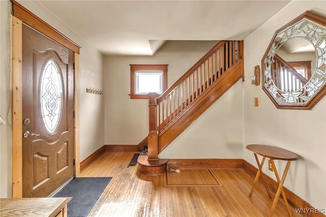 entryway featuring baseboards, light wood finished floors, and stairs