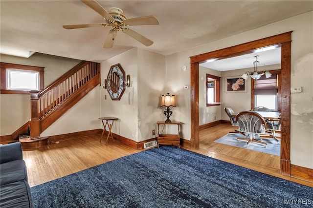 living area featuring visible vents, stairway, wood finished floors, baseboards, and ceiling fan with notable chandelier