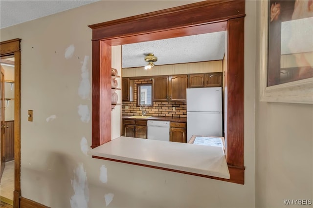 kitchen featuring light countertops, backsplash, a sink, a textured ceiling, and white appliances