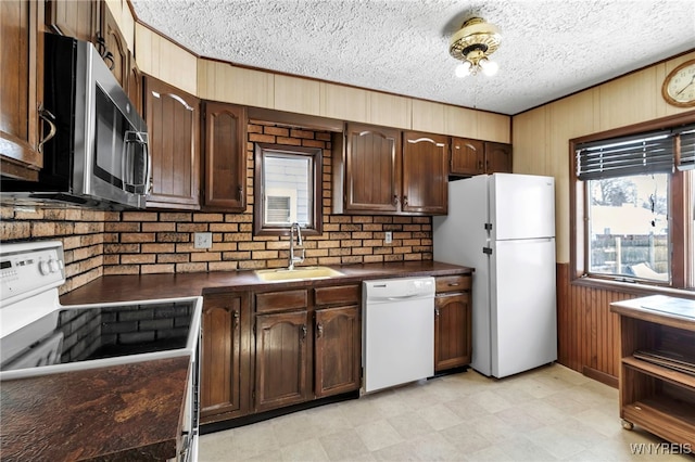 kitchen featuring white appliances, wood walls, dark countertops, and a sink