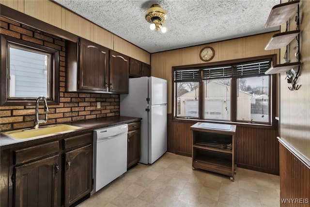 kitchen with white appliances, wooden walls, dark countertops, a textured ceiling, and a sink