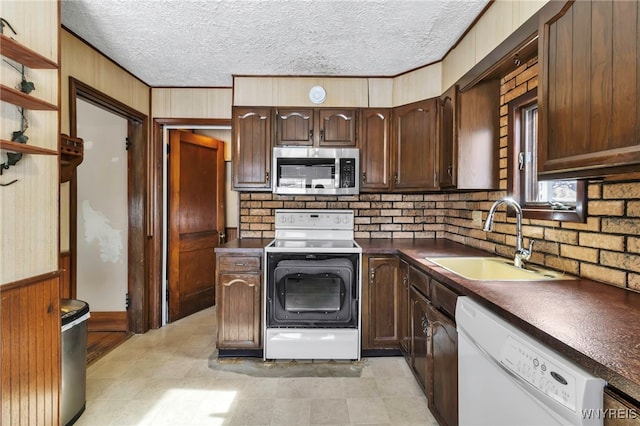 kitchen featuring dark countertops, a sink, wooden walls, a textured ceiling, and white appliances