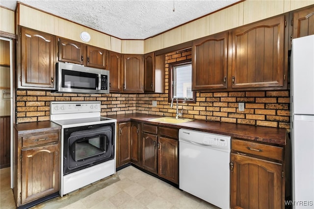 kitchen with light floors, dark countertops, a sink, a textured ceiling, and white appliances