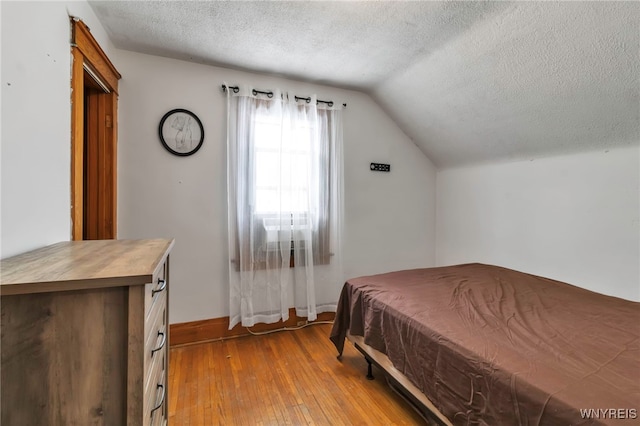 bedroom with vaulted ceiling, a textured ceiling, and light wood-type flooring