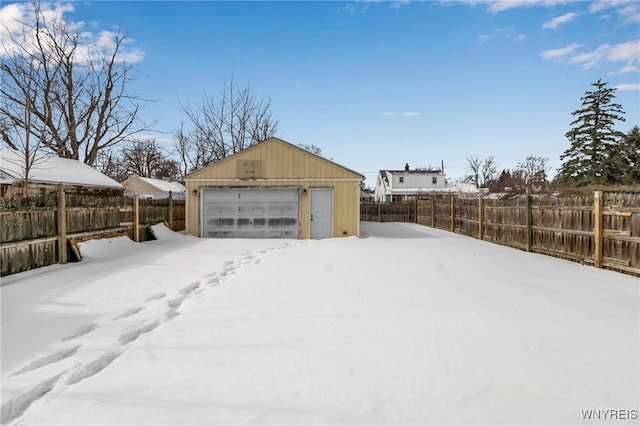 yard covered in snow with a garage, an outbuilding, and fence