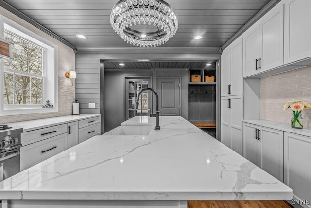 kitchen with wooden ceiling, a kitchen island with sink, light stone counters, and a sink