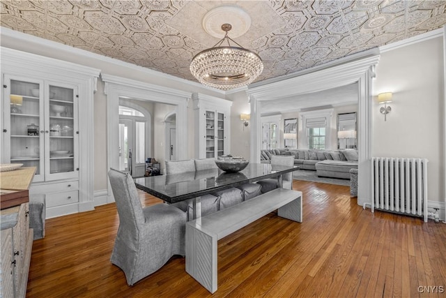 dining space featuring wood finished floors, ornamental molding, radiator, an ornate ceiling, and an inviting chandelier