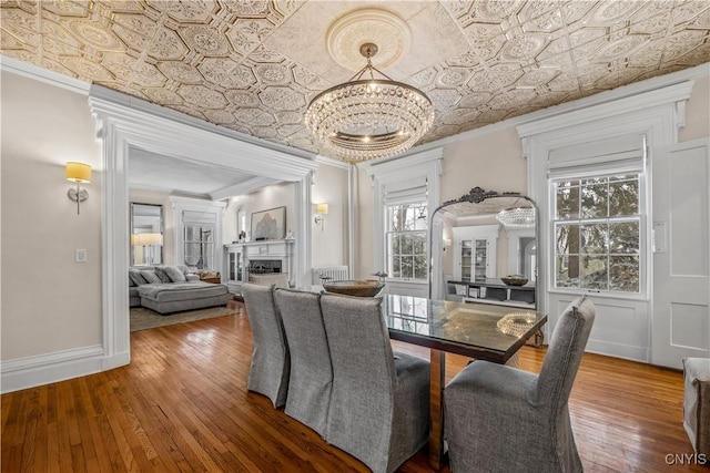 dining room featuring an ornate ceiling, wood finished floors, crown molding, a fireplace, and a notable chandelier