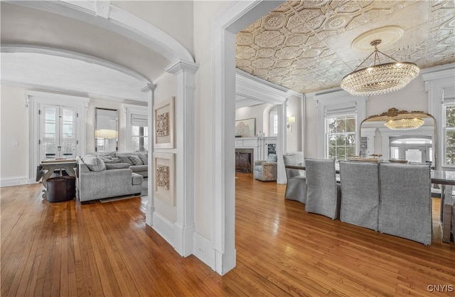 corridor with arched walkways, wood finished floors, an ornate ceiling, and crown molding