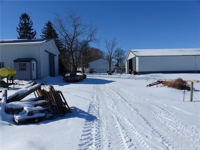 yard layered in snow featuring a garage and an outbuilding