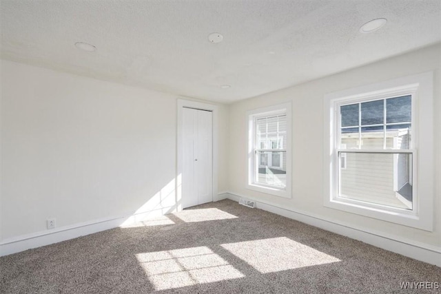 unfurnished room with baseboards, carpet, visible vents, and a textured ceiling