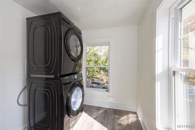 clothes washing area with laundry area, stacked washing maching and dryer, wood finished floors, and baseboards