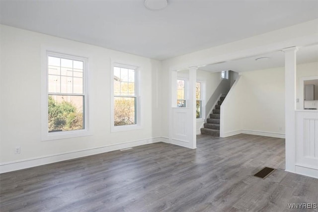 empty room featuring dark wood-type flooring, visible vents, baseboards, stairs, and ornate columns