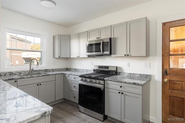 kitchen with stainless steel appliances, light stone counters, a sink, and gray cabinetry