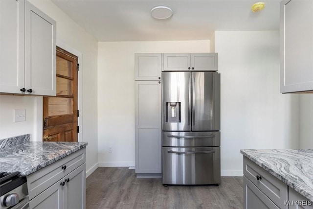 kitchen featuring light wood finished floors, stainless steel appliances, light stone counters, and baseboards