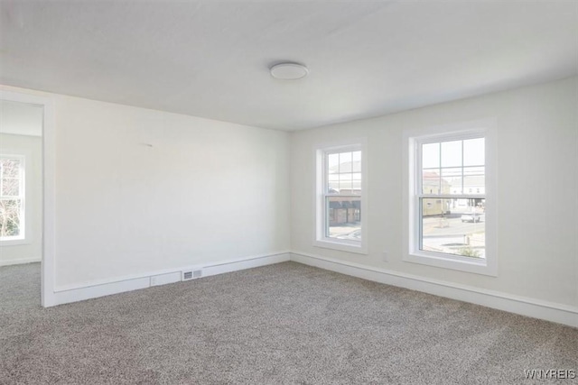 carpeted empty room featuring a wealth of natural light, visible vents, and baseboards