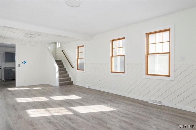 unfurnished room featuring a wainscoted wall, stairway, and light wood finished floors