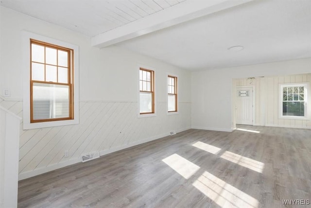 empty room featuring beam ceiling, a healthy amount of sunlight, and wood finished floors