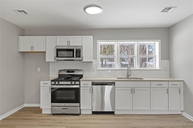 kitchen with appliances with stainless steel finishes, white cabinetry, a sink, and visible vents