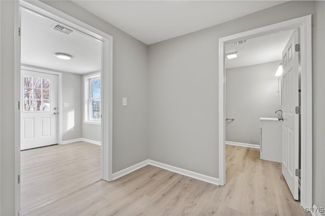 hallway featuring light wood-style floors, visible vents, a sink, and baseboards