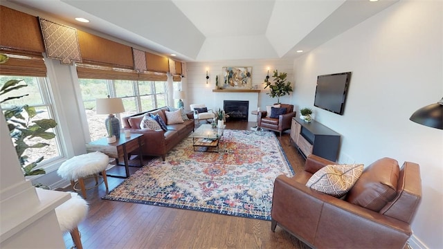 living room featuring a tray ceiling, dark wood-style flooring, a glass covered fireplace, and recessed lighting