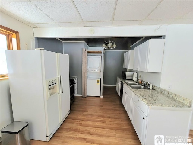 kitchen with a sink, white cabinets, stacked washing maching and dryer, white fridge with ice dispenser, and stainless steel microwave