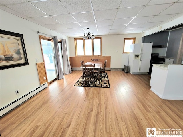 dining space with a baseboard radiator, baseboard heating, an inviting chandelier, light wood-style floors, and a drop ceiling