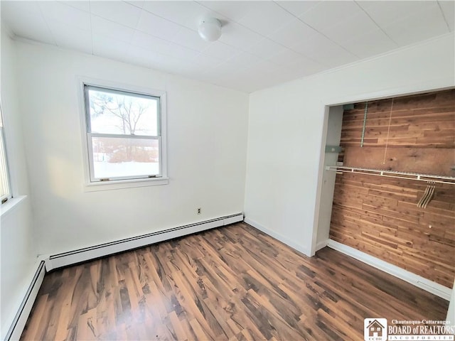 unfurnished bedroom featuring wooden walls, baseboards, baseboard heating, and wood finished floors