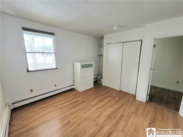 unfurnished bedroom featuring baseboard heating, light wood-type flooring, and a closet