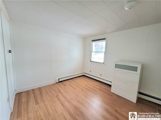 unfurnished bedroom with a baseboard heating unit, light wood-type flooring, baseboards, and baseboard heating