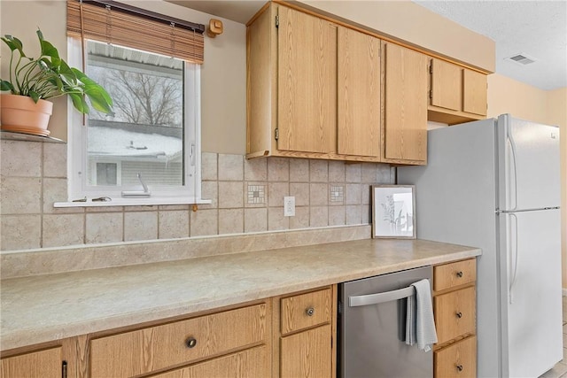 kitchen featuring tasteful backsplash, light countertops, stainless steel dishwasher, light brown cabinetry, and freestanding refrigerator