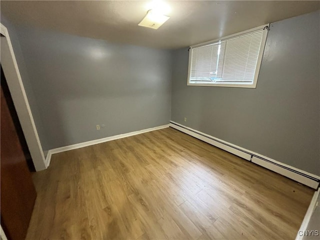 empty room with a baseboard heating unit, wood finished floors, and baseboards