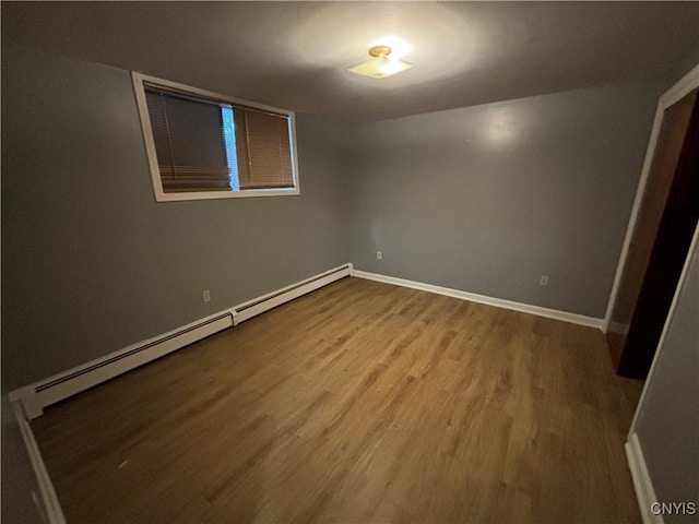 empty room featuring a baseboard radiator, baseboards, and wood finished floors