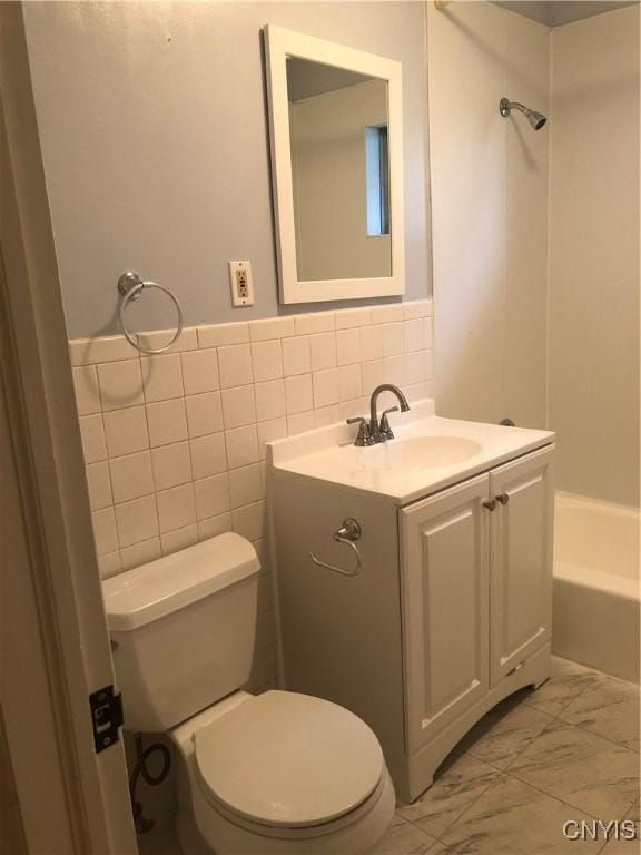 full bath featuring marble finish floor, tile walls, toilet, vanity, and a tub