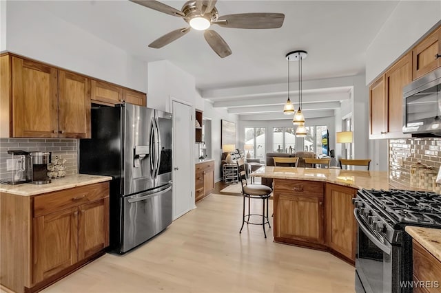 kitchen with brown cabinetry, appliances with stainless steel finishes, open floor plan, a kitchen breakfast bar, and hanging light fixtures