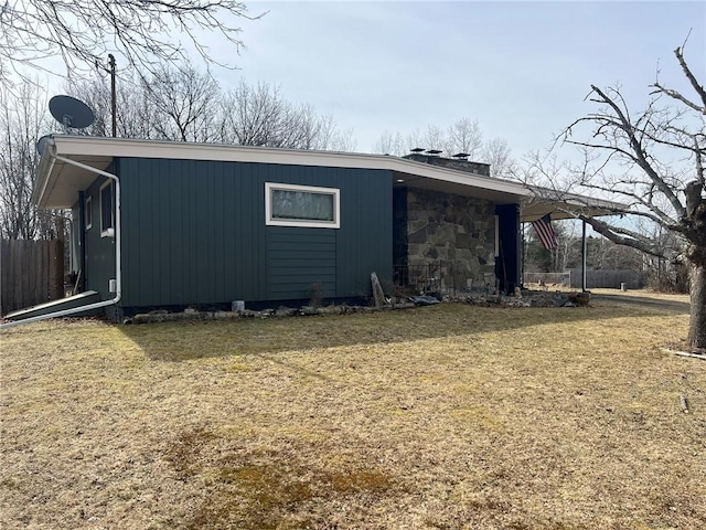 view of side of home with stone siding, a lawn, and fence