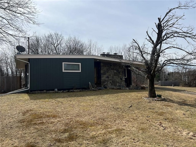 view of property exterior with stone siding, a lawn, a chimney, and fence