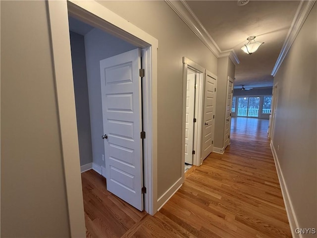 corridor featuring light wood finished floors, ornamental molding, and baseboards