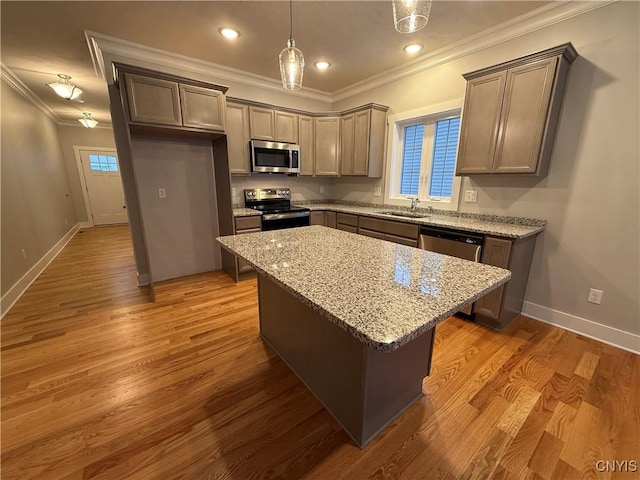 kitchen with light stone counters, wood finished floors, a kitchen island, appliances with stainless steel finishes, and pendant lighting