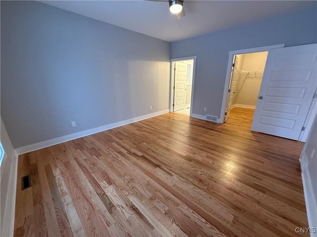 unfurnished bedroom featuring a walk in closet, baseboards, visible vents, and light wood finished floors