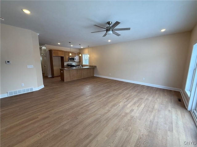 unfurnished living room featuring a ceiling fan, visible vents, baseboards, and wood finished floors