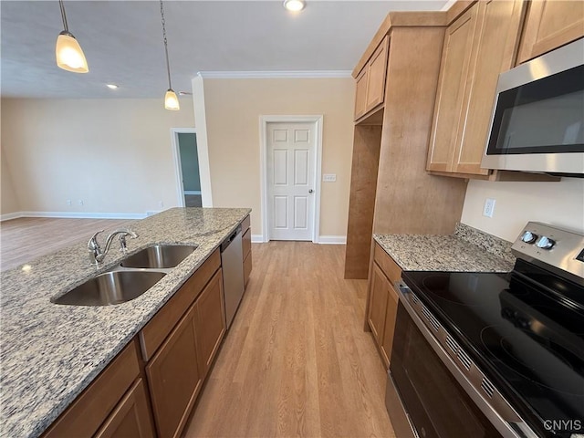 kitchen featuring light stone counters, a sink, hanging light fixtures, appliances with stainless steel finishes, and light wood finished floors