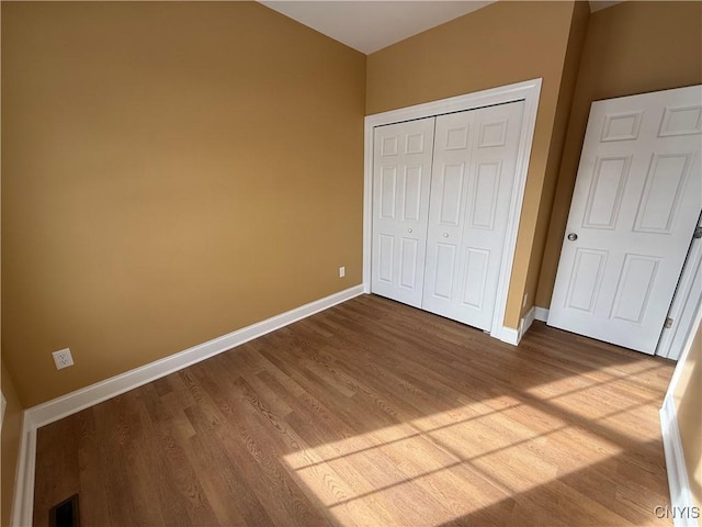 unfurnished bedroom with a closet, wood finished floors, visible vents, and baseboards