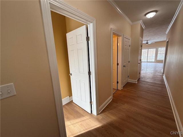 corridor featuring baseboards, wood finished floors, visible vents, and crown molding