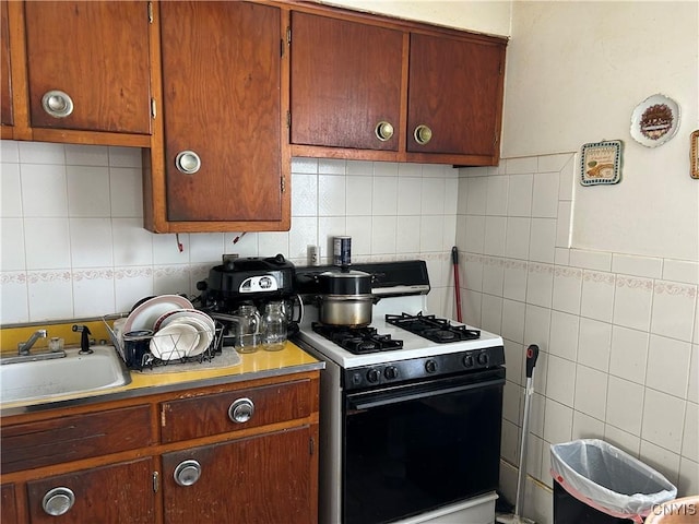 kitchen with range with gas cooktop, light countertops, a sink, and tile walls