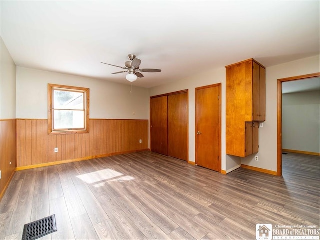 unfurnished bedroom with multiple closets, a wainscoted wall, visible vents, and wood finished floors