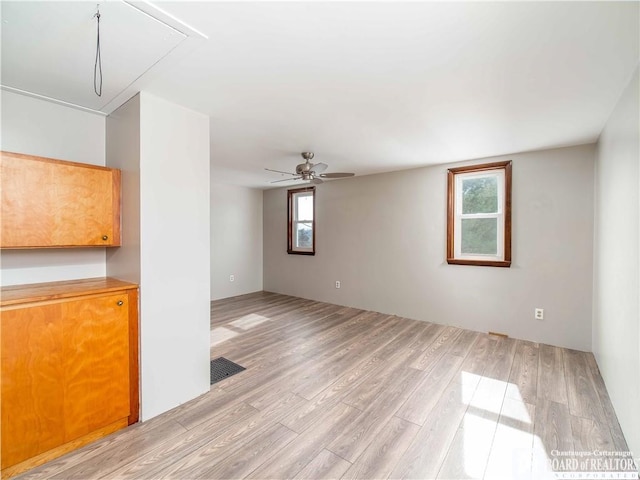 unfurnished room featuring light wood-type flooring, attic access, visible vents, and a ceiling fan